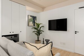 Ein modernes Wohnzimmer mit einer Couch, einem Flachbildfernseher, einer Topfpflanze und einem Bild an der Wand.