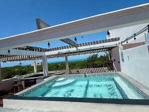 Ein Pool auf dem Dach mit Blick auf den Ozean, umgeben von einer Pergola mit hängenden Lichtern.