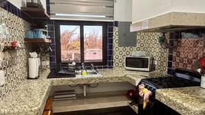 A compact kitchen with a microwave, stove, sink, and a window overlooking a residential area. - Cozy 1-bedroom studio in perfect Isla Mujeres with AC (Isla Mujeres)