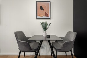 A minimalist room with a table and two chairs, a framed artwork above the table, and a potted plant on the table. - Station House | Stylish Apartment |No loadshedding (Cape Town)