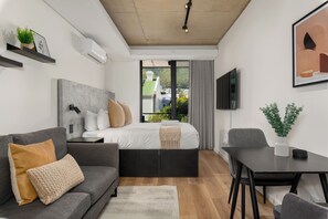 Ein modernes Schlafzimmer mit Bett, Sofa, Schreibtisch und Blick auf eine grüne Landschaft.