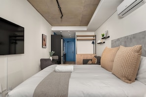 Un dormitorio moderno con una cama grande, un televisor de pantalla plana, un escritorio integrado y una puerta azul que da a un baño.