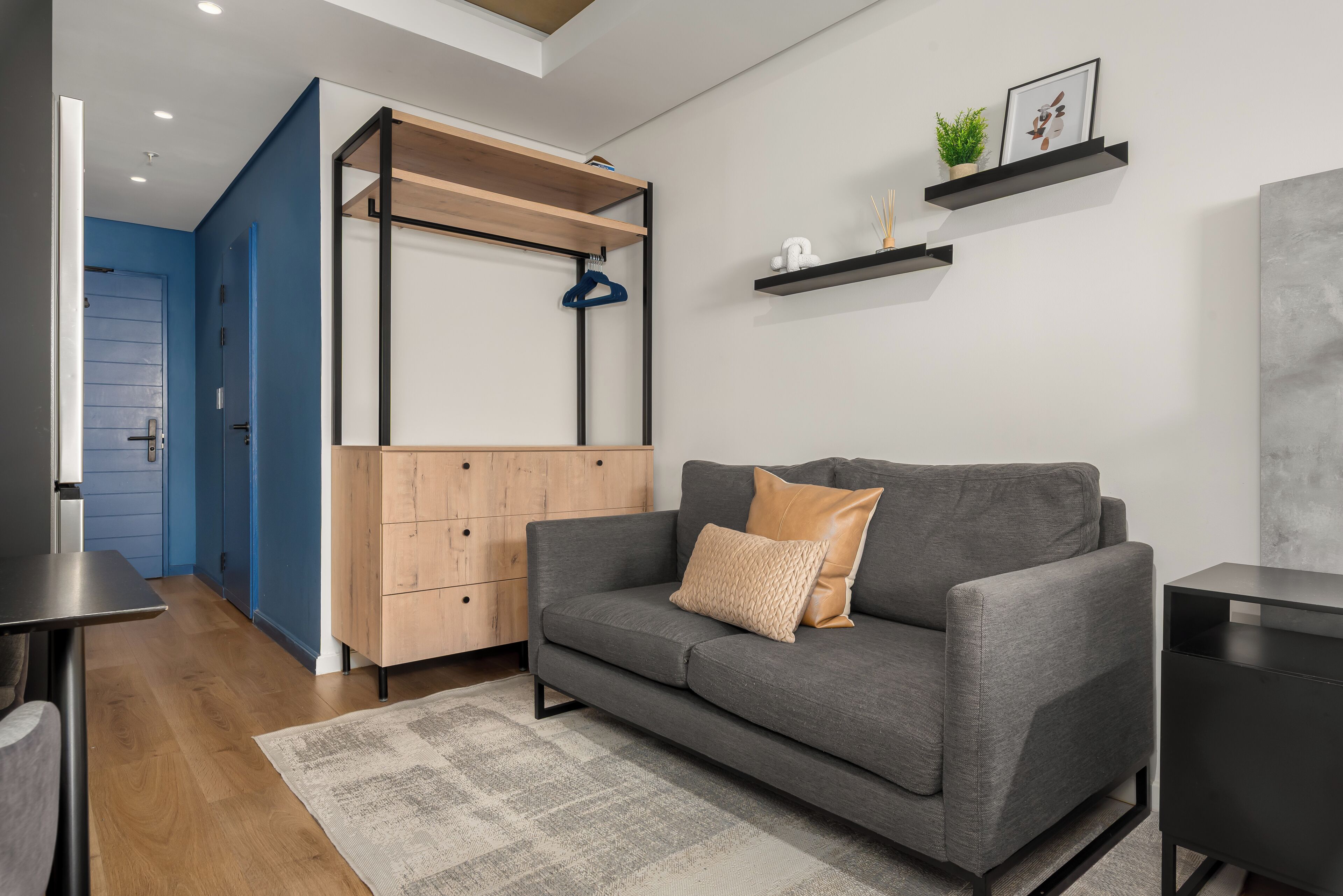 A modern living room with a grey sofa, a wooden cabinet, and a blue door.