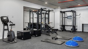 Une salle de sport équipée de matériel d’exercice, notamment un tapis de course, des appareils de musculation et des tapis de sol.