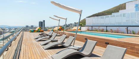 Une terrasse ensoleillée avec des chaises longues et une piscine.