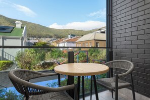 Ein Balkon mit Korbstühlen und einem kleinen runden Tisch, mit Blick auf eine Stadt mit Gebäuden und einer Hügelkette in der Ferne.