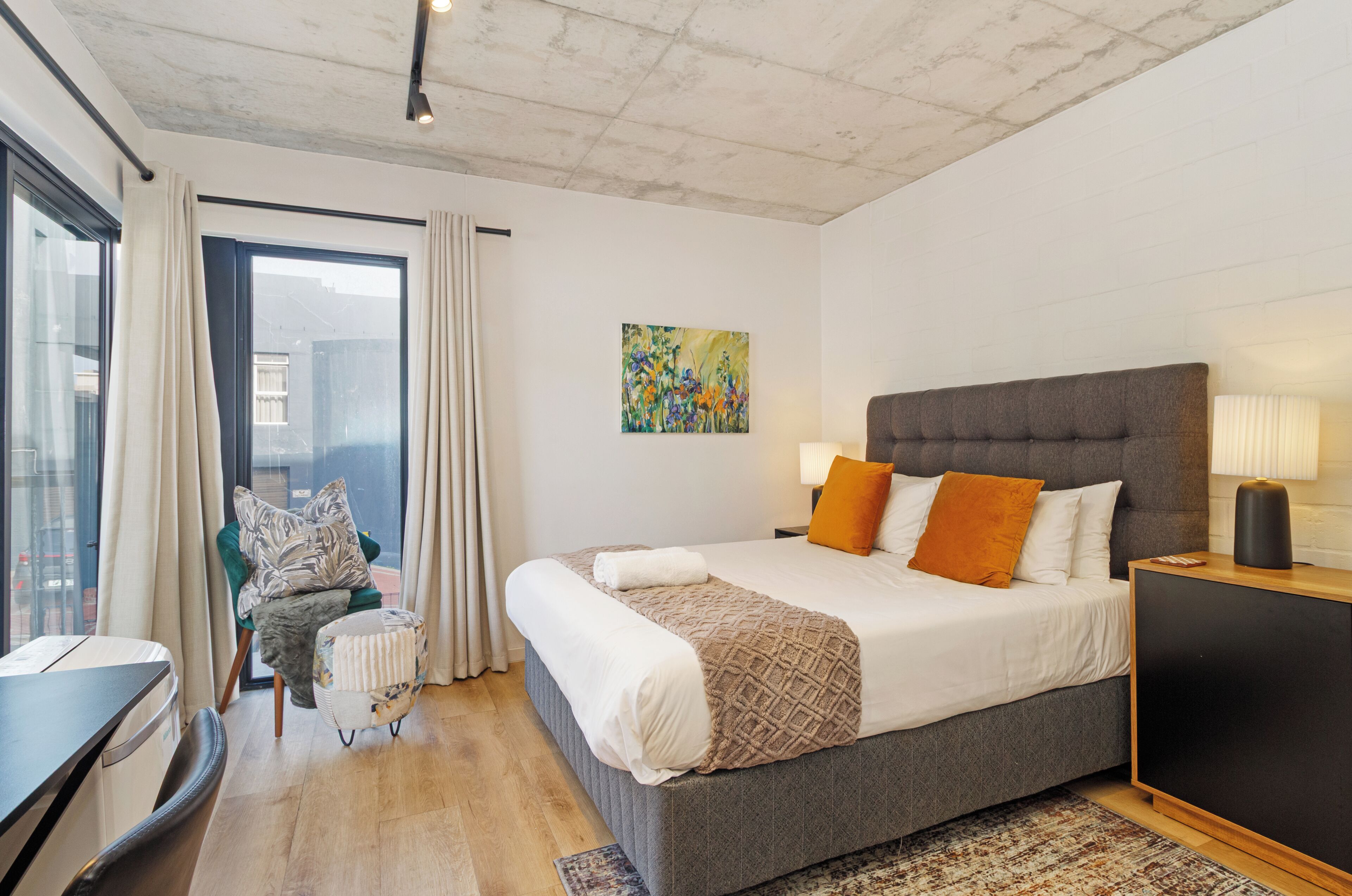 Una habitación de hotel moderna con una cama grande, un pequeño rincón de descanso y vistas a la ciudad.