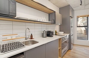 A modern kitchen with a built-in dishwasher, a coffee machine, and a view of the street through a window. - Stylish Sea Point Studio (Cape Town)