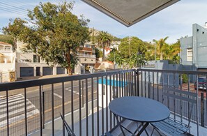 A balcony with a table and chairs, overlooking a street with cars and buildings. - Stylish Sea Point Studio (Cape Town)