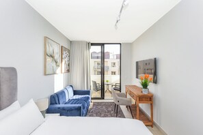Une chambre d’hôtel comprenant un lit, un canapé, un bureau, une chaise, une télévision et un balcon avec vue sur les bâtiments.