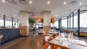 A modern restaurant with high ceilings, large windows, and a mix of seating arrangements including tables and booths. - One Rosebank | Elevated Urban Comfort (Johannesburg)