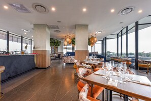 A modern restaurant with high ceilings, large windows, and a mix of seating arrangements including tables and booths. - One Rosebank | Elevated Urban Comfort (Johannesburg)