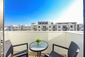 A balcony with a table and chairs, a potted plant, and a view of a row of buildings. - One Rosebank | Elevated Urban Comfort (Johannesburg)