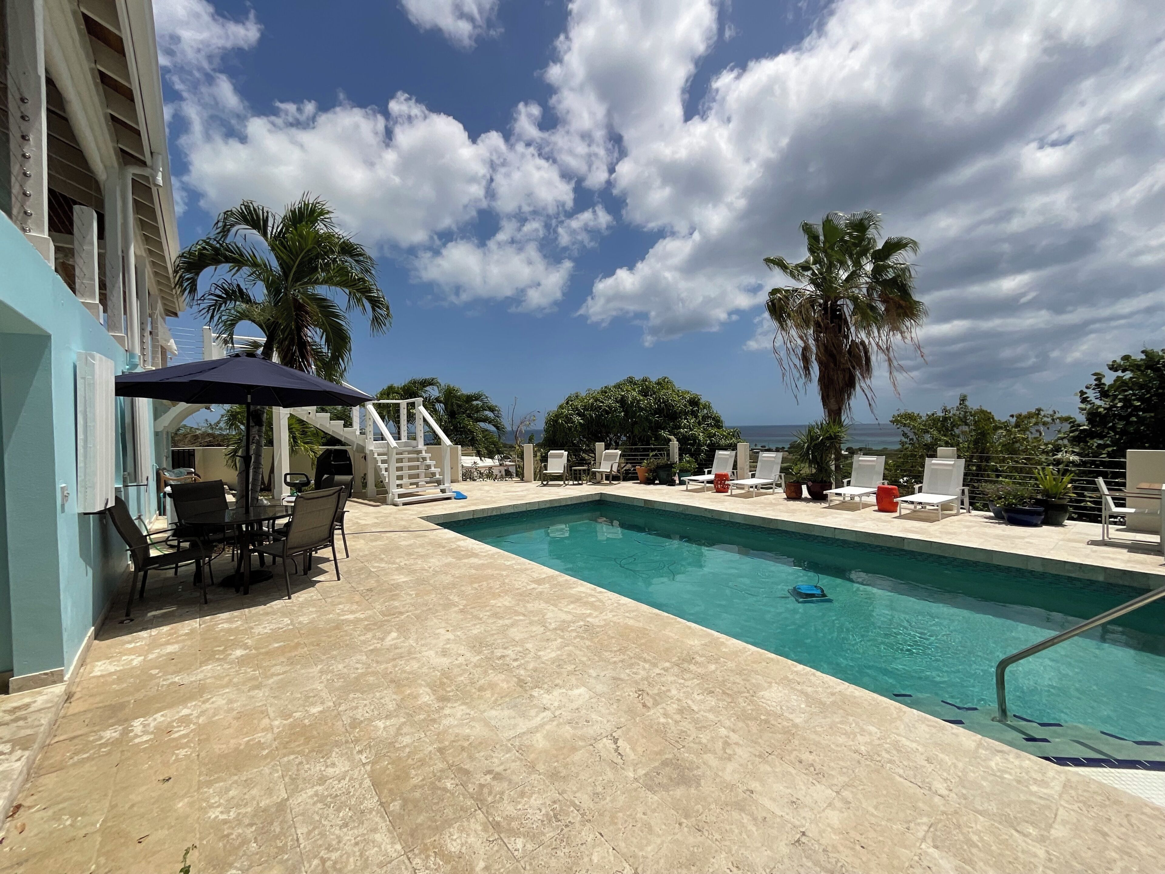 Une piscine avec une terrasse carrelée, des chaises longues et des palmiers.