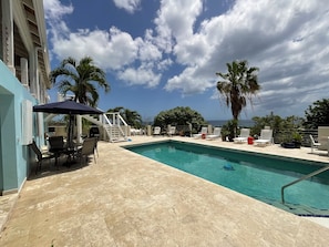 A swimming pool with a tiled deck, lounge chairs, and palm trees. - Lovely 1-bedroom with AC and pool in charming Frederiksted new to the market! (Frederiksted)