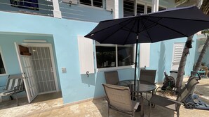A patio with a table and chairs, a black umbrella, and a door with a metal gate.