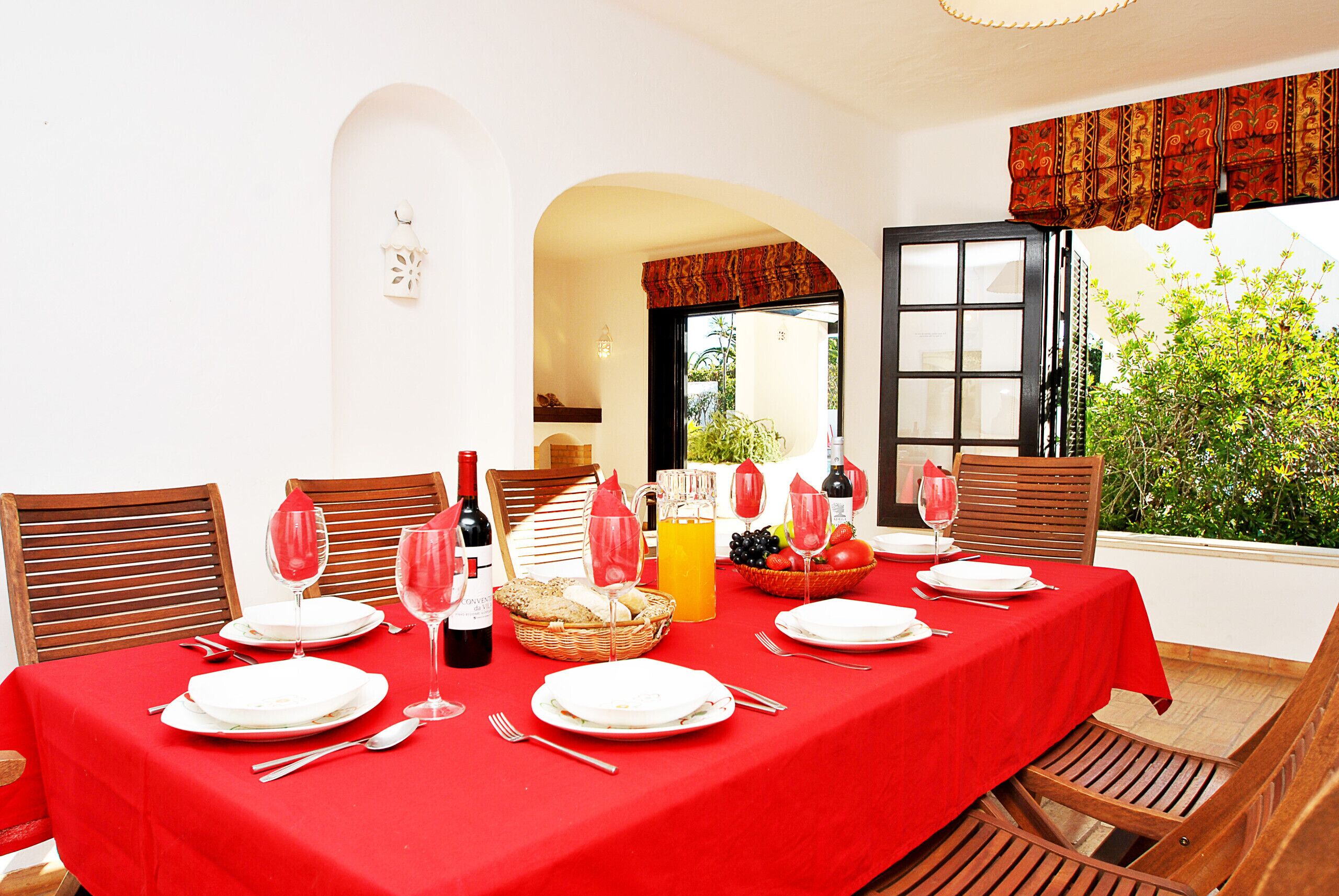 A dining table set for six with red tablecloth, white plates, and various glassware.