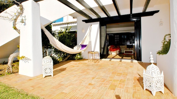 A modern outdoor patio with a hammock, white lanterns, and a view into a living area. - Villa with Pool and BBQ near Galé Beach (Albufeira)