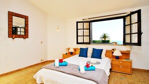 A bedroom with a bed, a nightstand, a lamp, a mirror, and an open window with a view. - Villa with Pool and BBQ near Galé Beach (Albufeira)