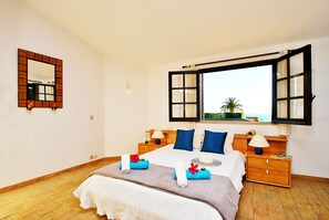 A bedroom with a bed, a nightstand, a lamp, a mirror, and an open window with a view. - Villa with Pool and BBQ near Galé Beach (Albufeira)