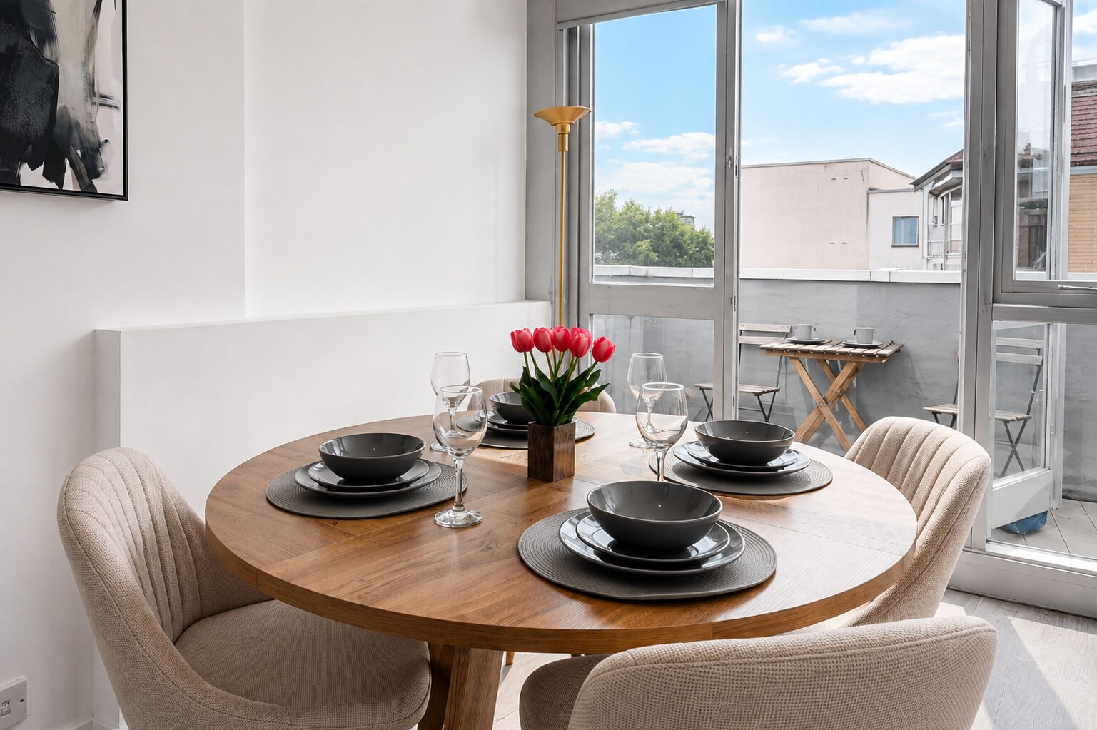 Une table de salle à manger ronde, avec des assiettes et des bols noirs, entourée de chaises de couleur beige, dressée pour quatre personnes.