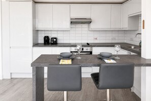 Eine moderne Küche mit weißen Schränken, einer dunklen Arbeitsplatte und zwei Barhocker.
