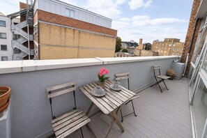 Eine Dachterrasse mit Holztisch und -stühlen, einem Blumentopf und Blick auf umliegende Gebäude.