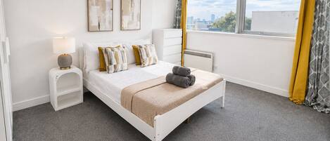 A bedroom with a bed, bedside tables, a lamp, a radiator, and a window with curtains.