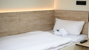 Una cama bien hecha con sábanas y almohadas blancas, un control remoto en la mesita de noche y un cabecero de madera.