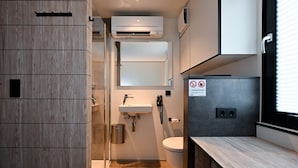 Un baño moderno con ducha, lavamanos e inodoro. Hay un perchero, un espejo y un cartel que indica prohibido fumar.