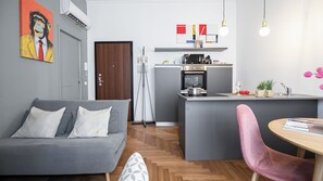Une cuisine moderne avec un îlot central, un canapé gris et une chaise rose.