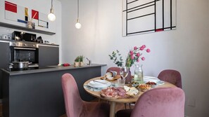 A modern kitchen with a dining area featuring a round table set with food and drinks, surrounded by pink chairs. - Italianway Easy - Tunisia 42 (Milan)