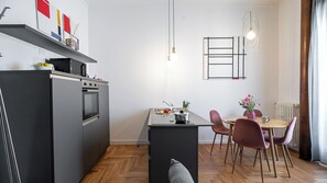 Une cuisine moderne dotée d’un four encastré, d’un coin repas avec une table et des chaises, et d’un luminaire suspendu.