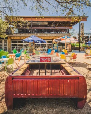 An outdoor seating area with colorful chairs and tables, a sign reading 'TRK YRD,' and a building with large windows in the background. - Home away from Home - Grill, Patio, Near Lake, Shops & Entertainment, The Colony (The Colony)