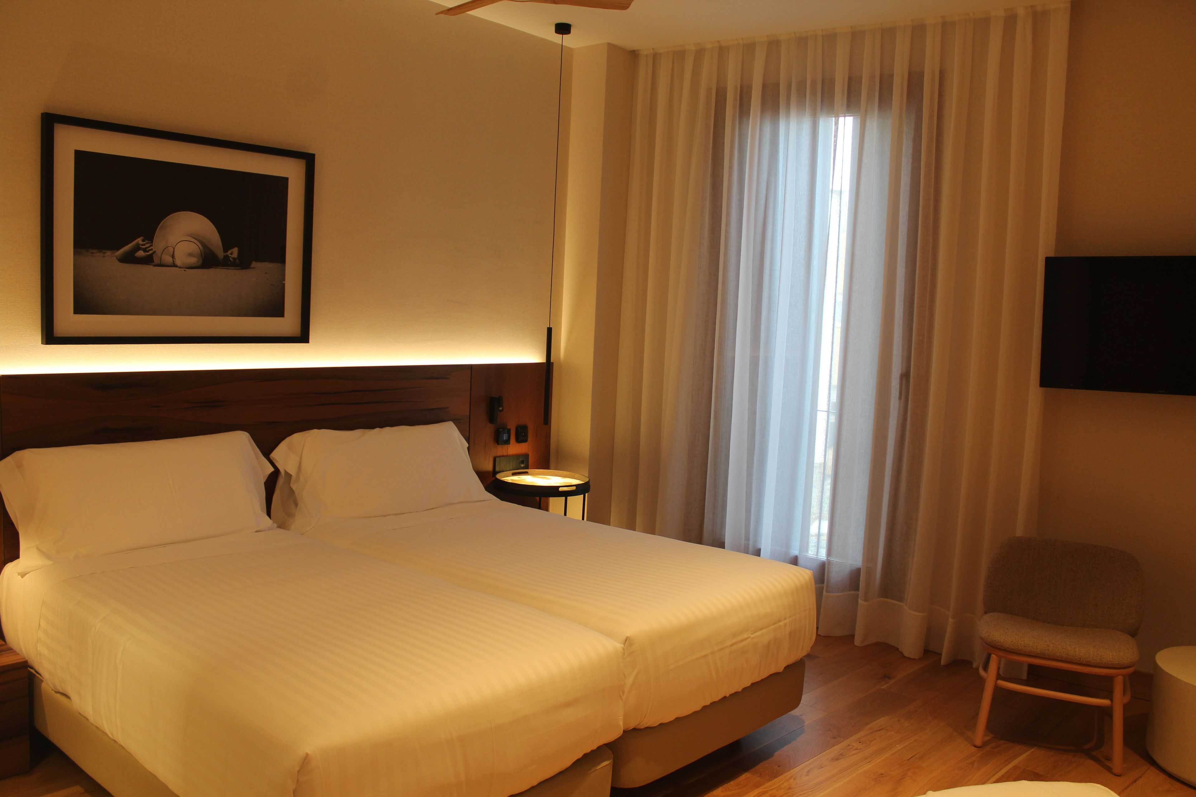 A hotel room with a large bed, a bedside table, a chair, a television, and a framed picture on the wall.