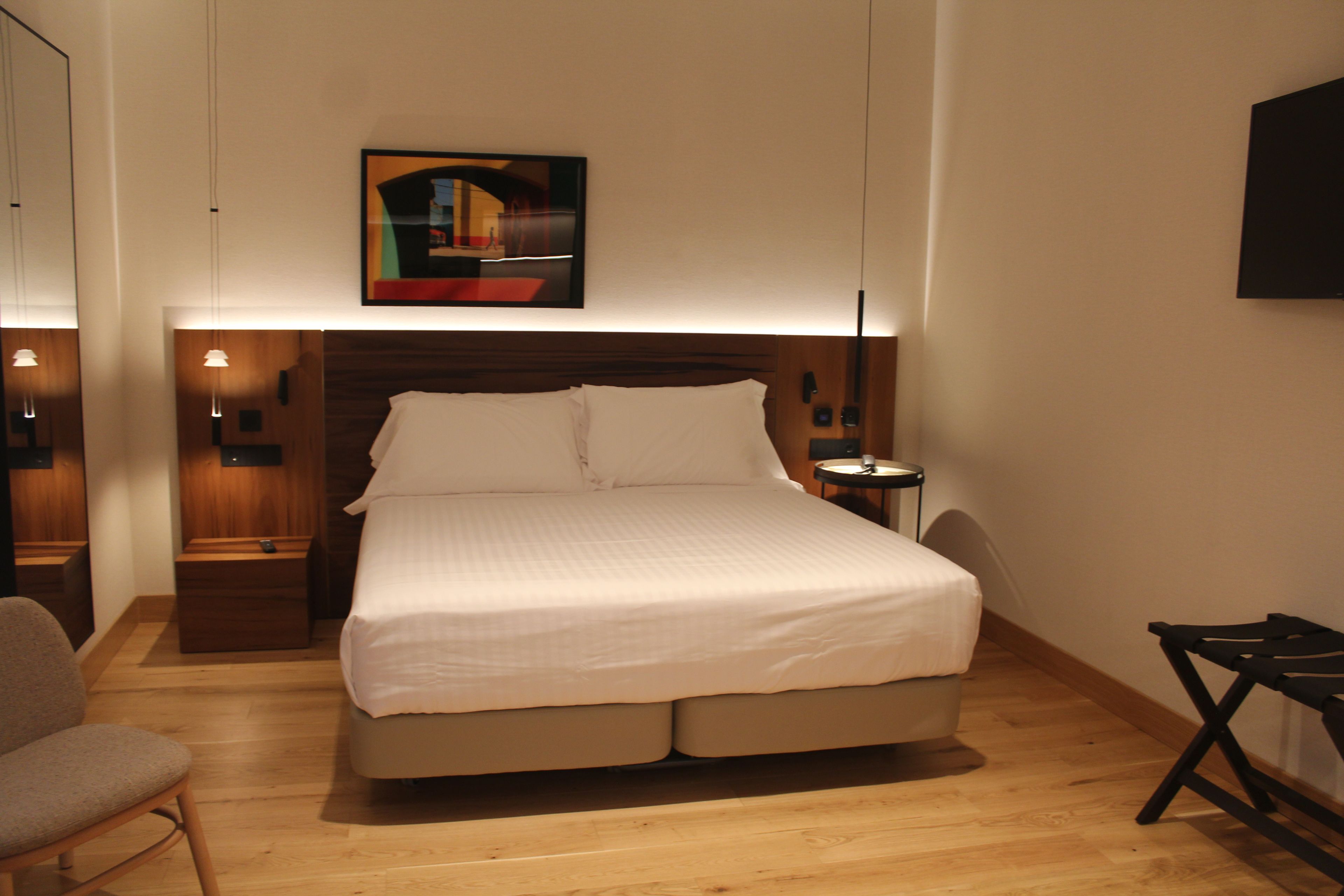 Ein Hotelzimmer mit einem großen Bett, Nachttischen, einem Sessel, einem Schreibtisch und einem Bild an der Wand.