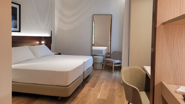 Een hotelkamer met een bed, een stoel, een bureau, een spiegel en een plafondventilator.