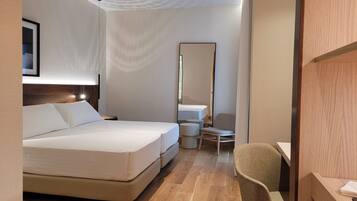 Una habitación de hotel con cama, una silla, un escritorio, un espejo y un ventilador de techo.