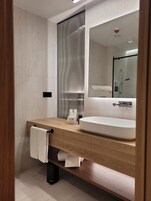 A modern bathroom with a wooden vanity, a large mirror, and a built-in shower.