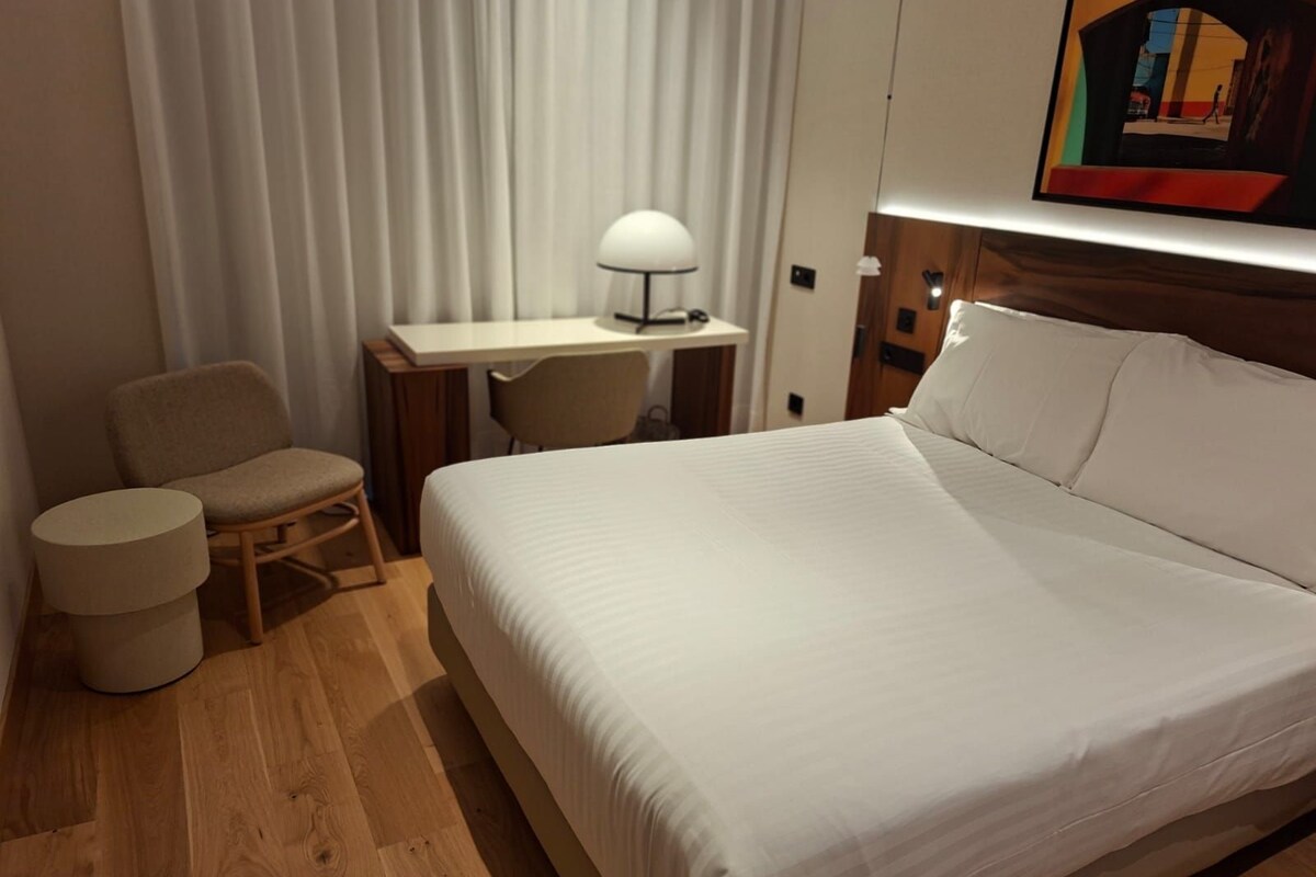 Et hotelværelse med en seng, et skrivebord, en stol og en lampe.