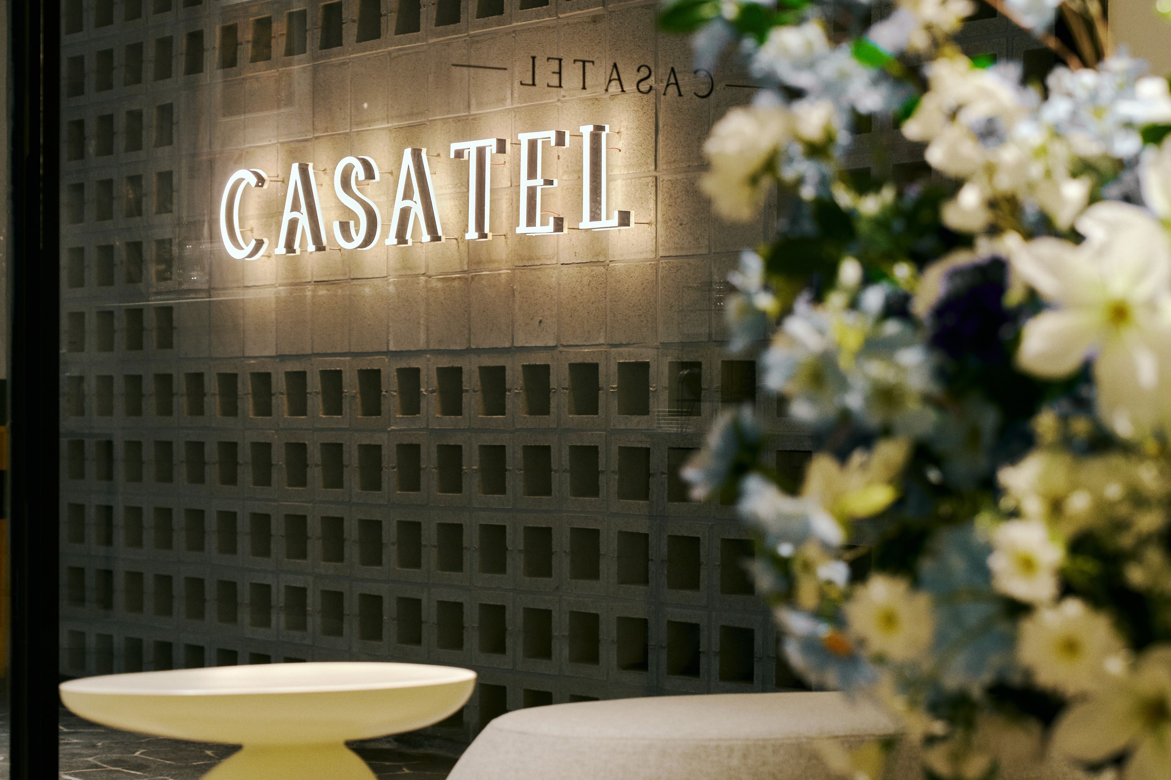 Un letrero de hotel con el nombre 'CASATEL' iluminado sobre una pared con diseño de cuadrícula.