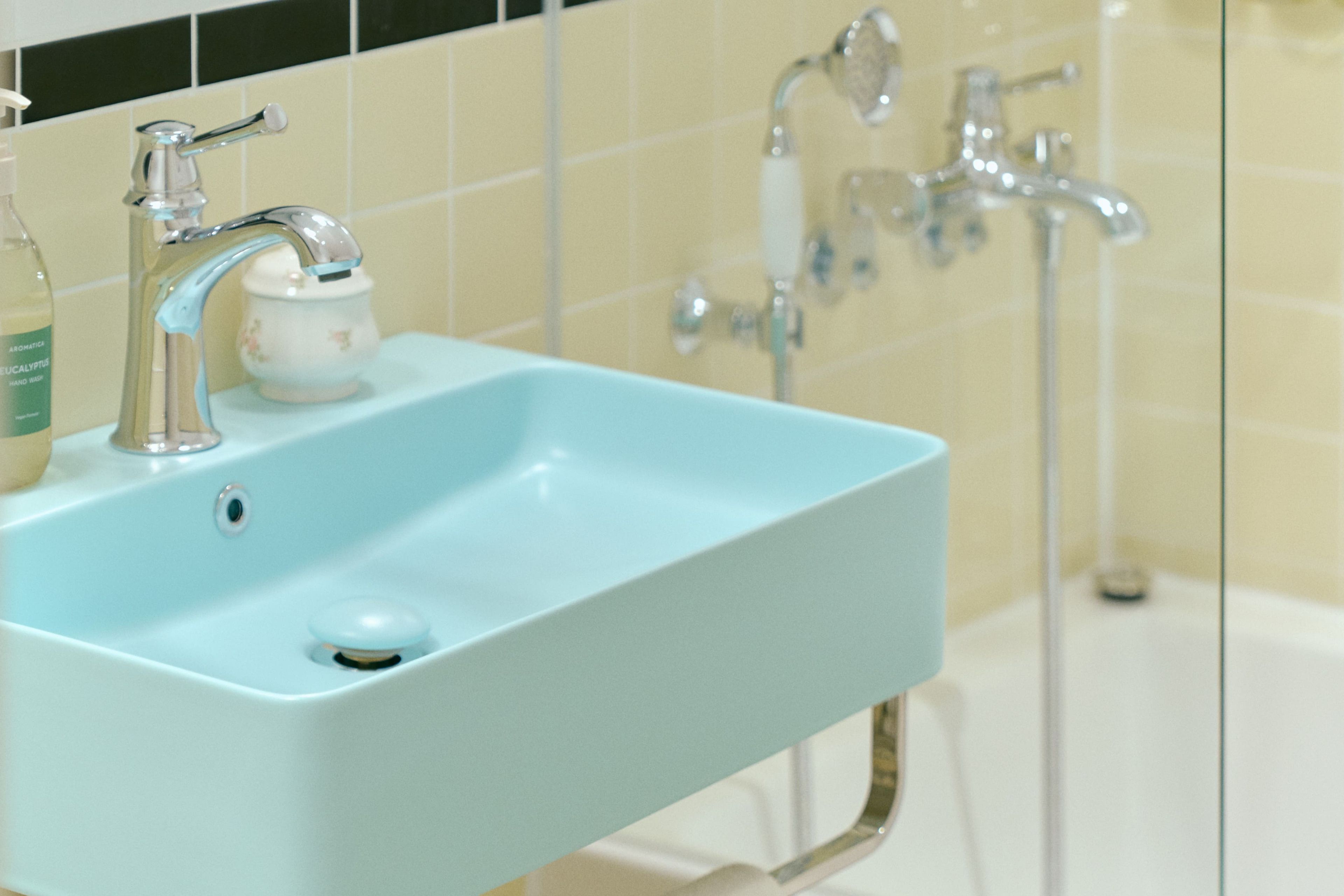 A bathroom with a light blue sink, a white cup, and a bottle of hand soap.
