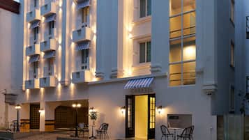 Un hotel con fachada blanca, varios balcones y una entrada a nivel de calle con asientos al aire libre.