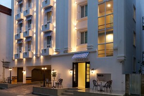A hotel with a white facade, multiple balconies, and a ground-level entrance with outdoor seating.