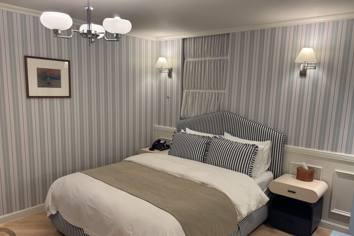 A neatly arranged bedroom with a bed, bedside lamps, a framed picture, and a bedside telephone.