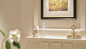 A white mantelpiece with a framed artwork, a white ceramic rabbit, a clear glass bottle, and two ornate glass pitchers. - Casatel Jeonju Hanok Village (Jeonju)