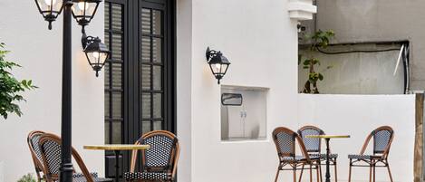 An outdoor seating area with wicker chairs and tables, a black door with the name 'CASATEL' above it, and wall-mounted lanterns.
