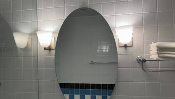 Een badkamer met een grote ovale spiegel, twee wandlampen, een handdoekhouder en een accentmuur met blauw en wit tegelwerk.