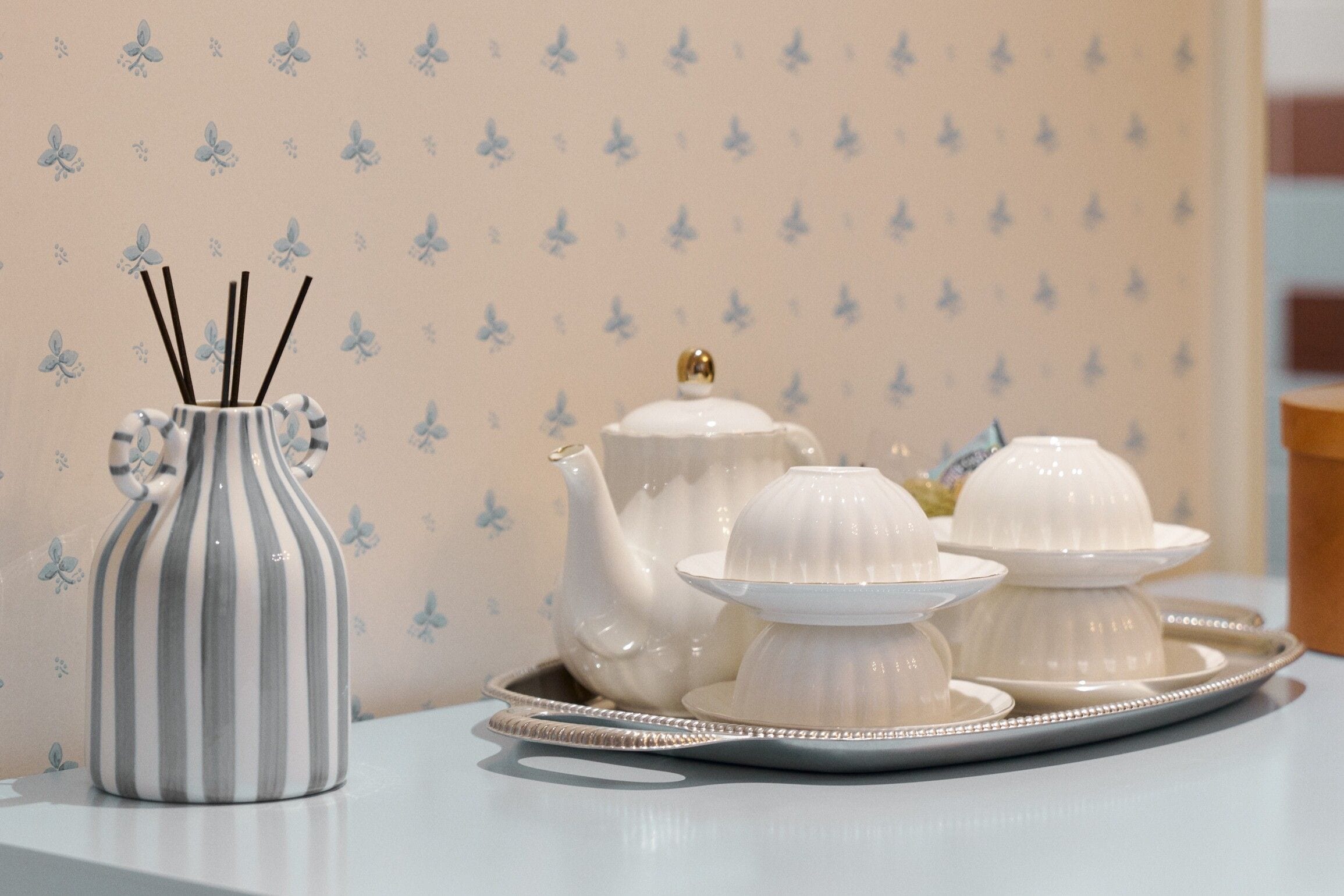 A table with a striped vase, a teapot, and two white sugar bowls on a tray.