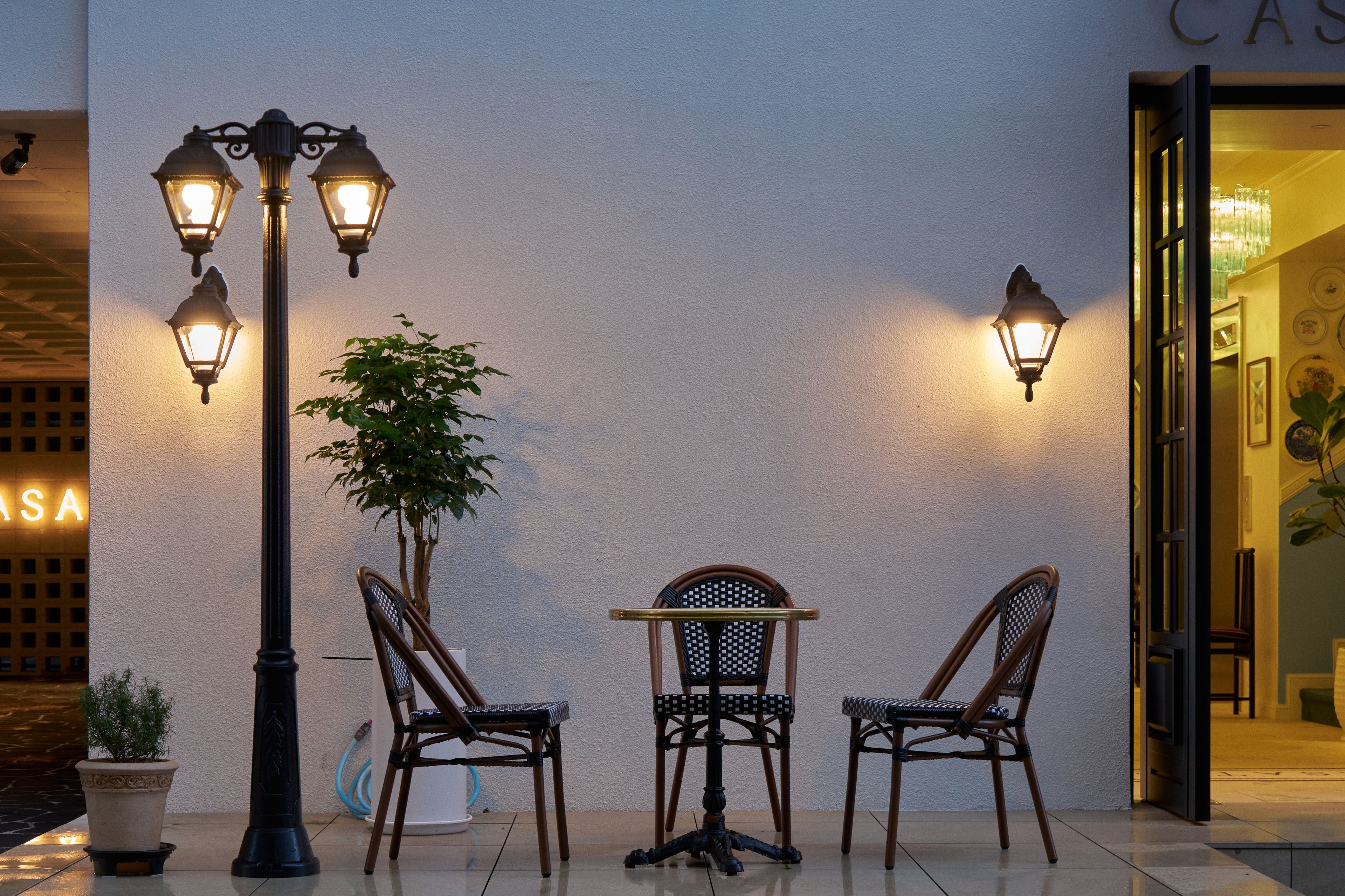 Een terras met twee rieten stoelen, een tafel, een lantaarnpaal en een potplant.